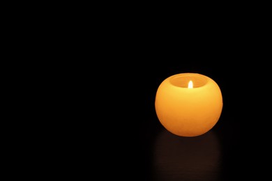 Photo of One round burning candle on black background, space for text