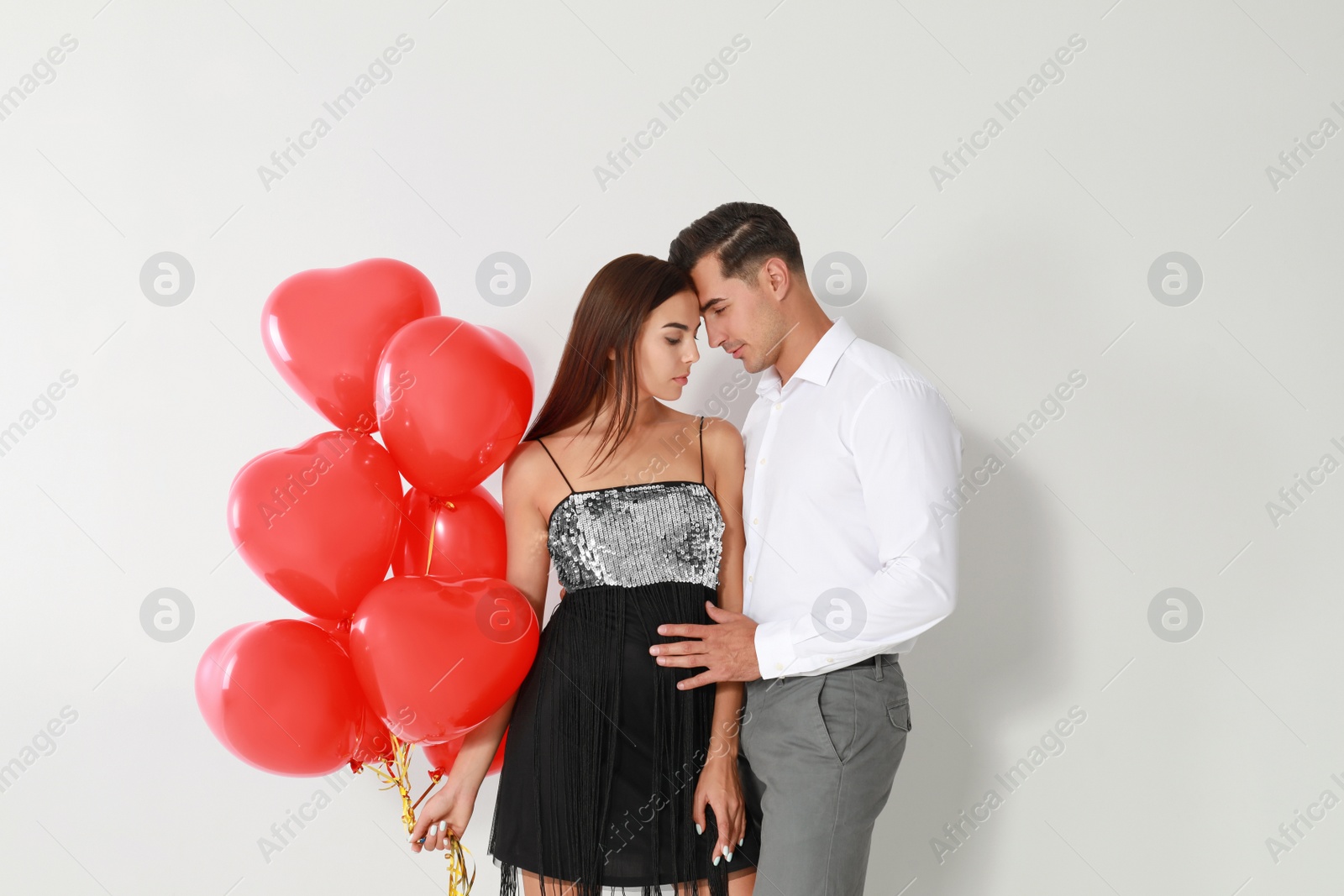 Photo of Beautiful couple with heart shaped balloons on light background