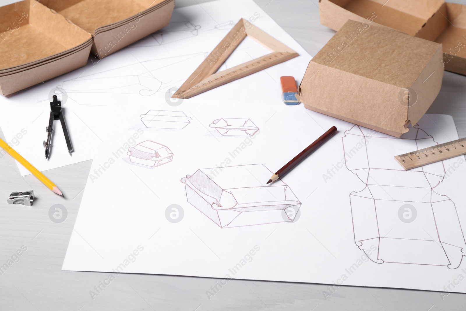 Photo of Creating packaging design. Drawings, boxes and stationery on light wooden table, closeup