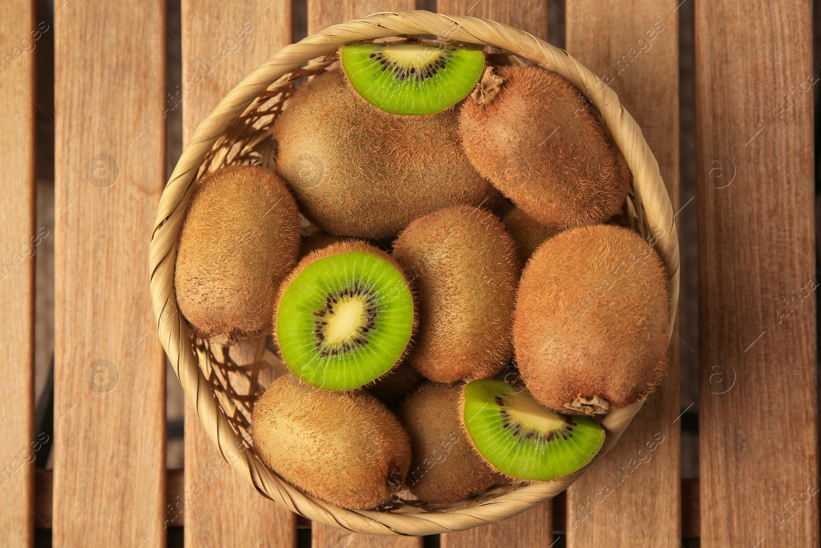 Photo of Wicker basket with whole and cut kiwis on wooden table, top view