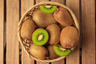 Wicker basket with whole and cut kiwis on wooden table, top view