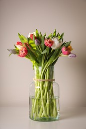 Photo of Beautiful bouquet of colorful tulips in glass vase on beige background