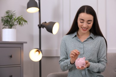 Young woman putting coin into piggy bank at home