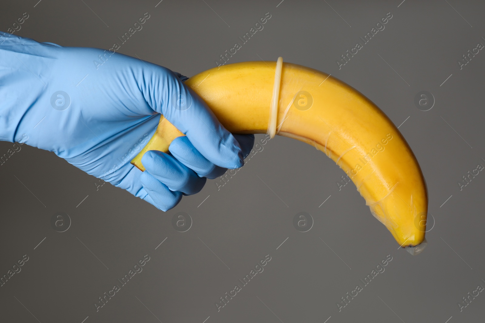 Photo of Doctor holding banana in condom symbolizing male sexual organ on grey background, closeup. Potency problem