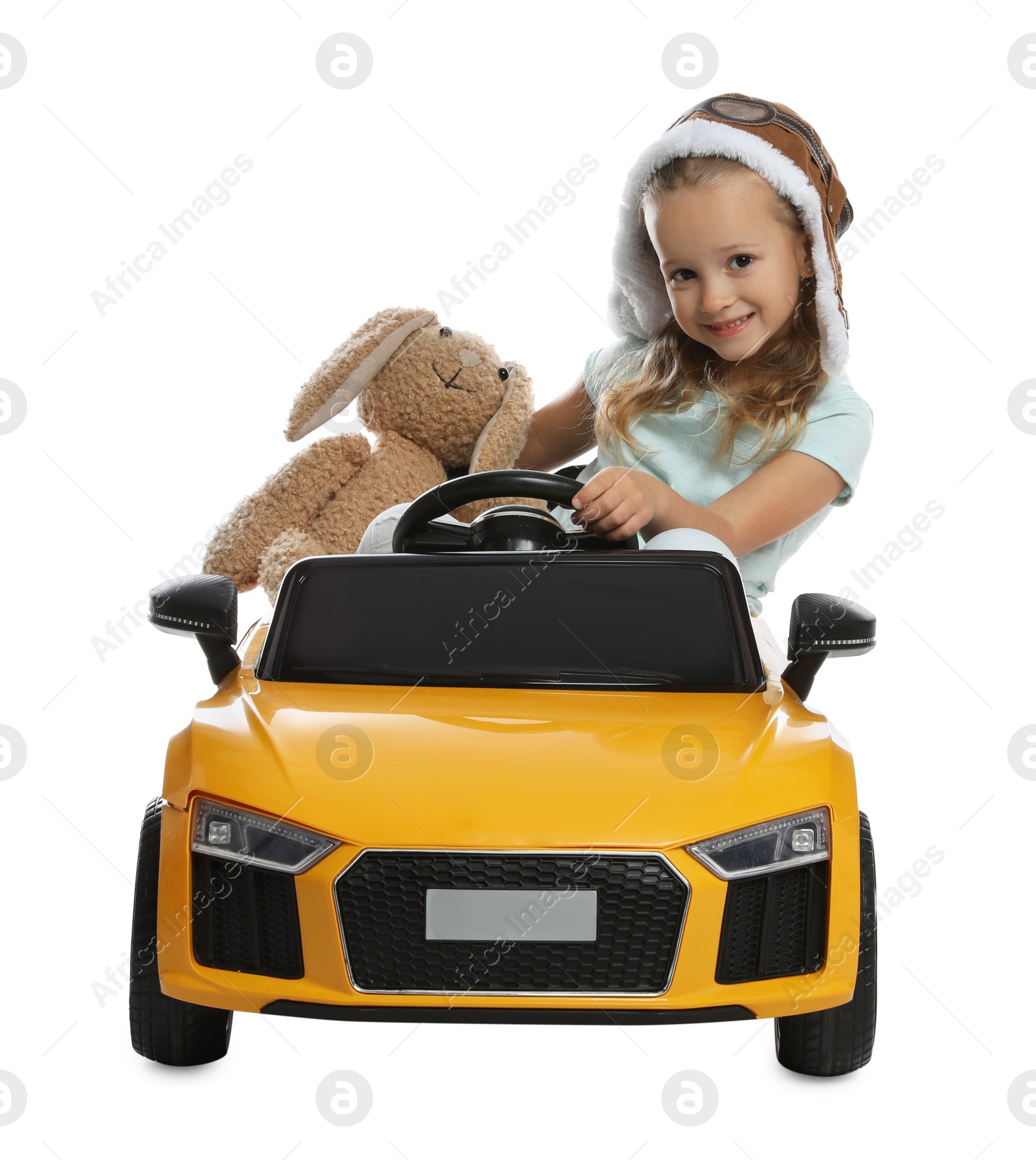 Photo of Cute little girl with toy bunny driving children's car on white background