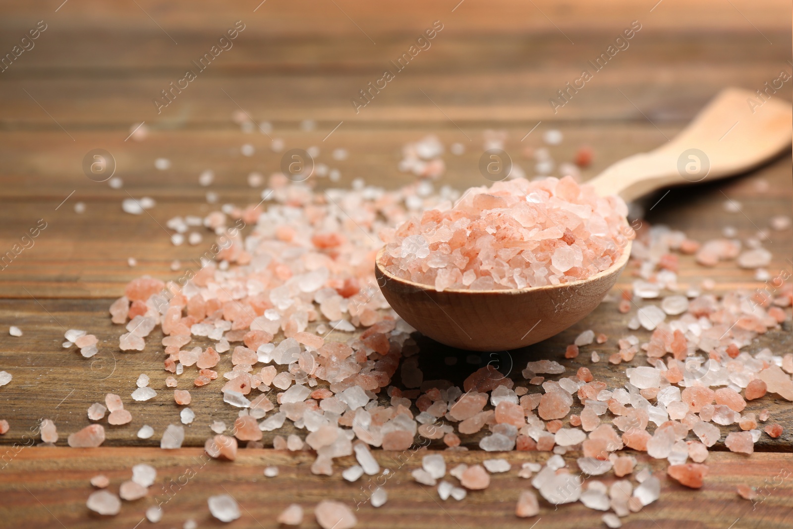 Photo of Pink himalayan salt and spoon on wooden table, closeup