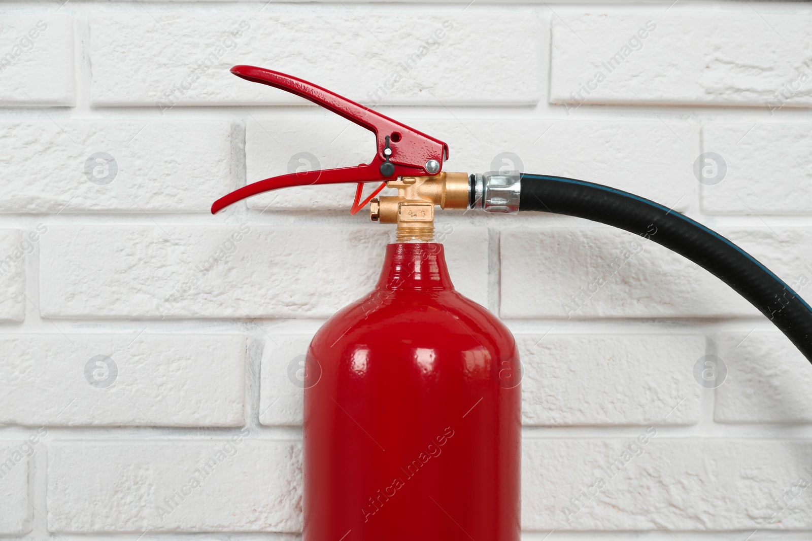 Photo of Fire extinguisher near white brick wall, closeup