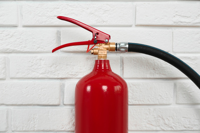 Photo of Fire extinguisher near white brick wall, closeup