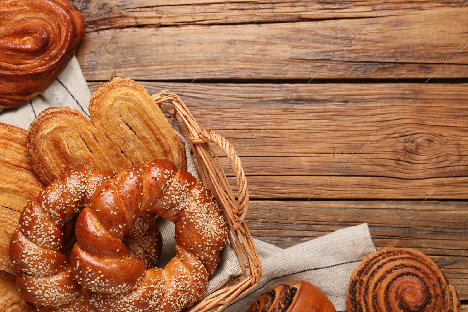 Photo of Wicker basket and different tasty freshly baked pastries on wooden table, flat lay. Space for text