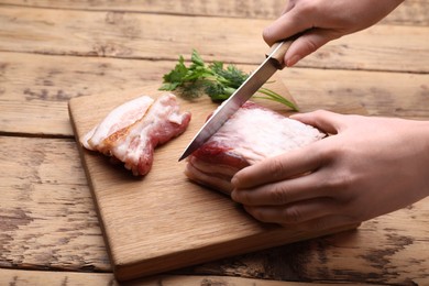 Photo of Woman cutting fresh pork fatback at wooden table, closeup