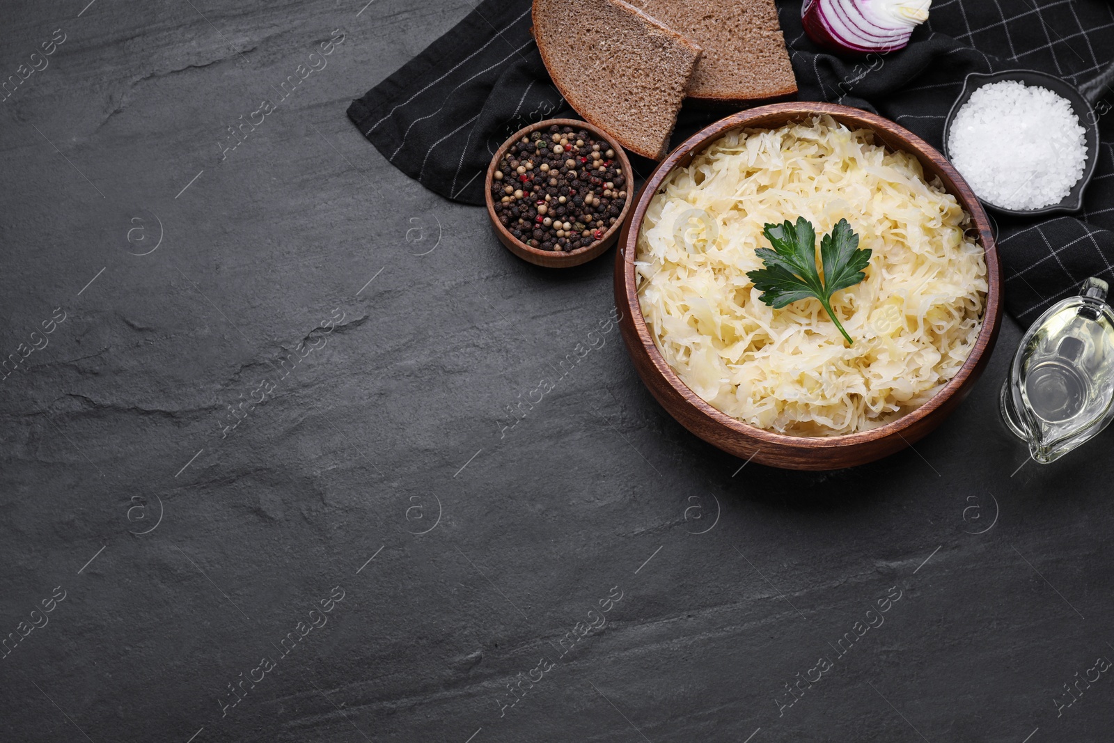 Photo of Bowl of tasty sauerkraut and ingredients on black table, flat lay. Space for text