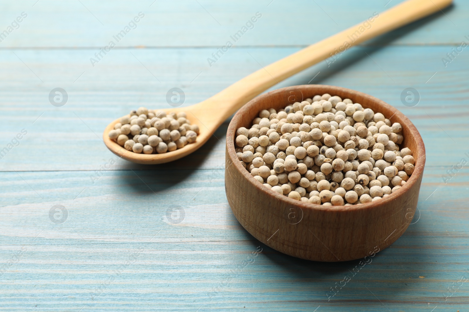 Photo of Aromatic spice. White pepper in bowl and spoon on light blue wooden table, closeup. Space for text