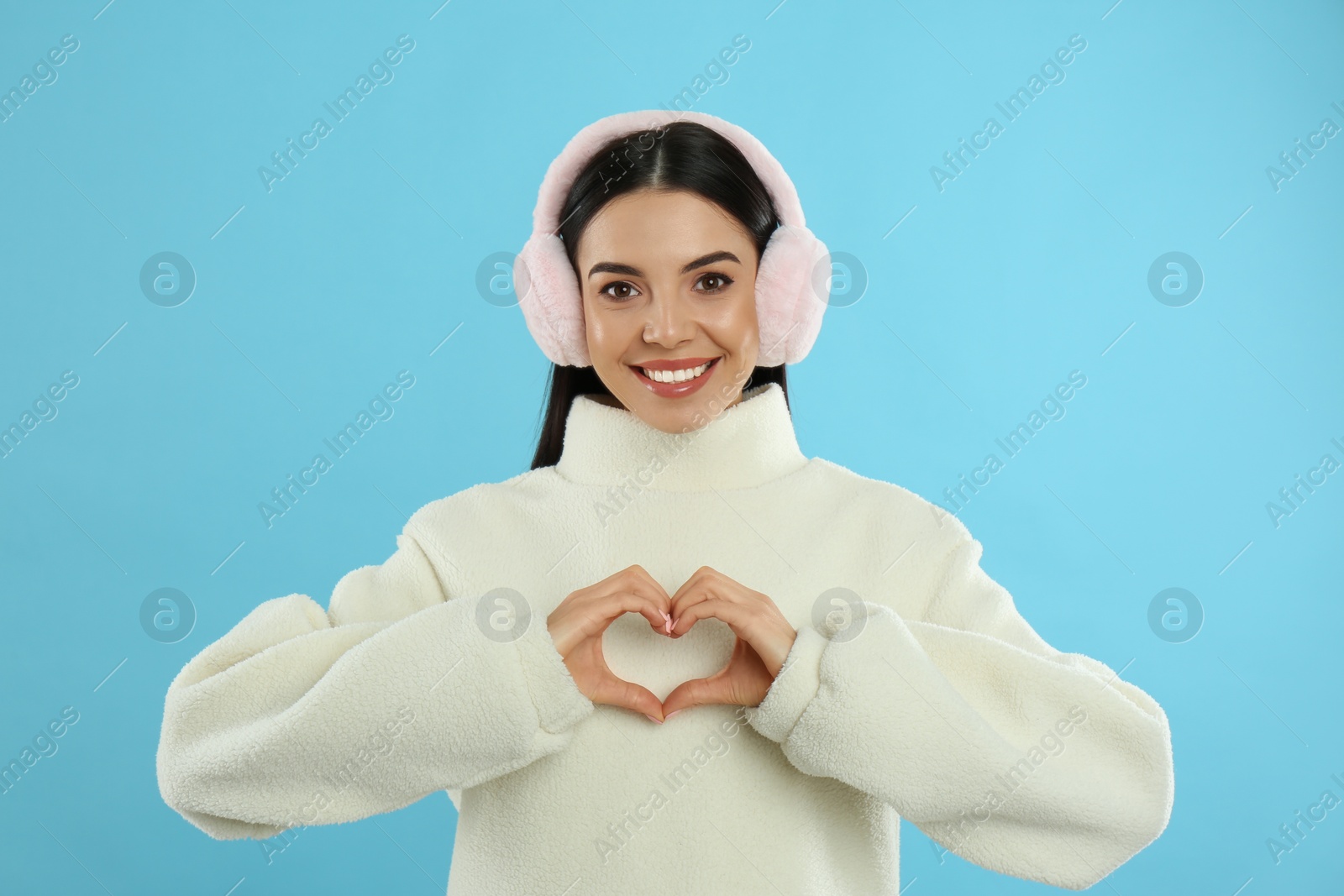 Photo of Beautiful young woman wearing earmuffs on light blue background