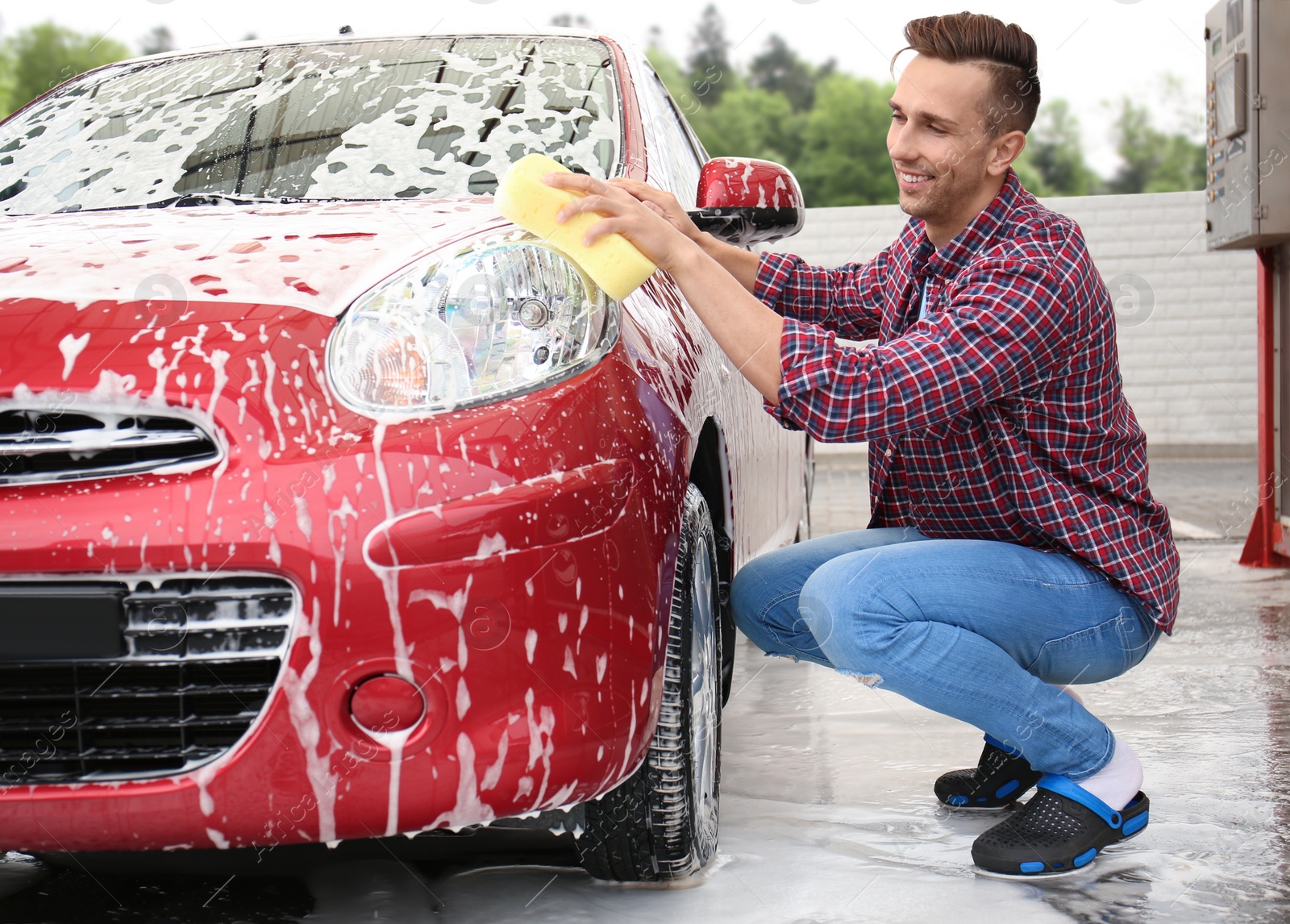 Photo of Young man cleaning vehicle with sponge at self-service car wash