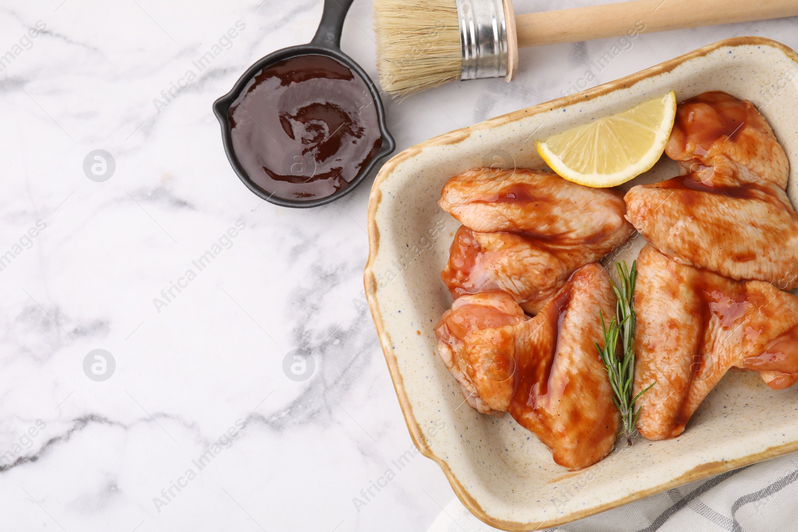 Photo of Fresh marinade, basting brush, raw chicken wings, rosemary and lemon on white marble table, flat lay. Space for text