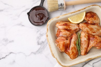 Fresh marinade, basting brush, raw chicken wings, rosemary and lemon on white marble table, flat lay. Space for text