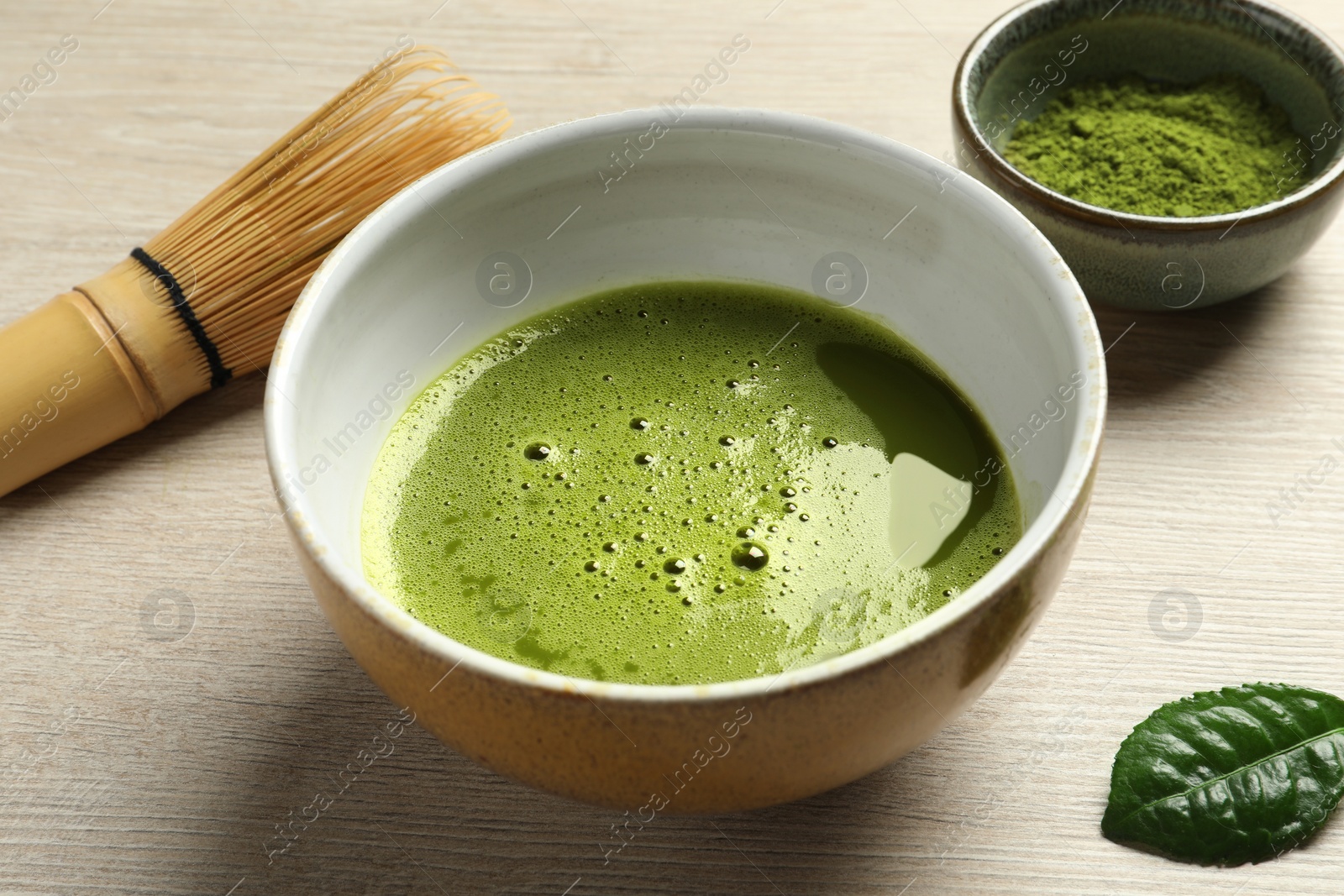 Photo of Cup of fresh matcha tea, bamboo whisk and green powder on white wooden table, closeup