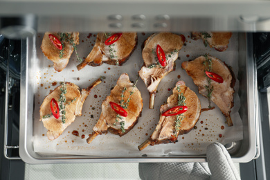 Chef taking baking tray with delicious ribs out of oven, top view