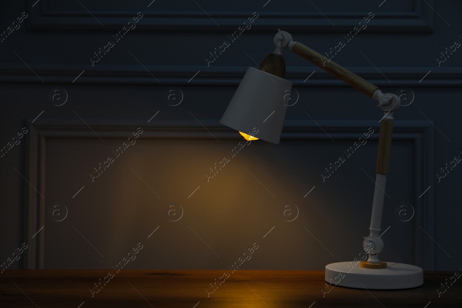 Photo of Stylish modern desk lamp on wooden table at night, space for text