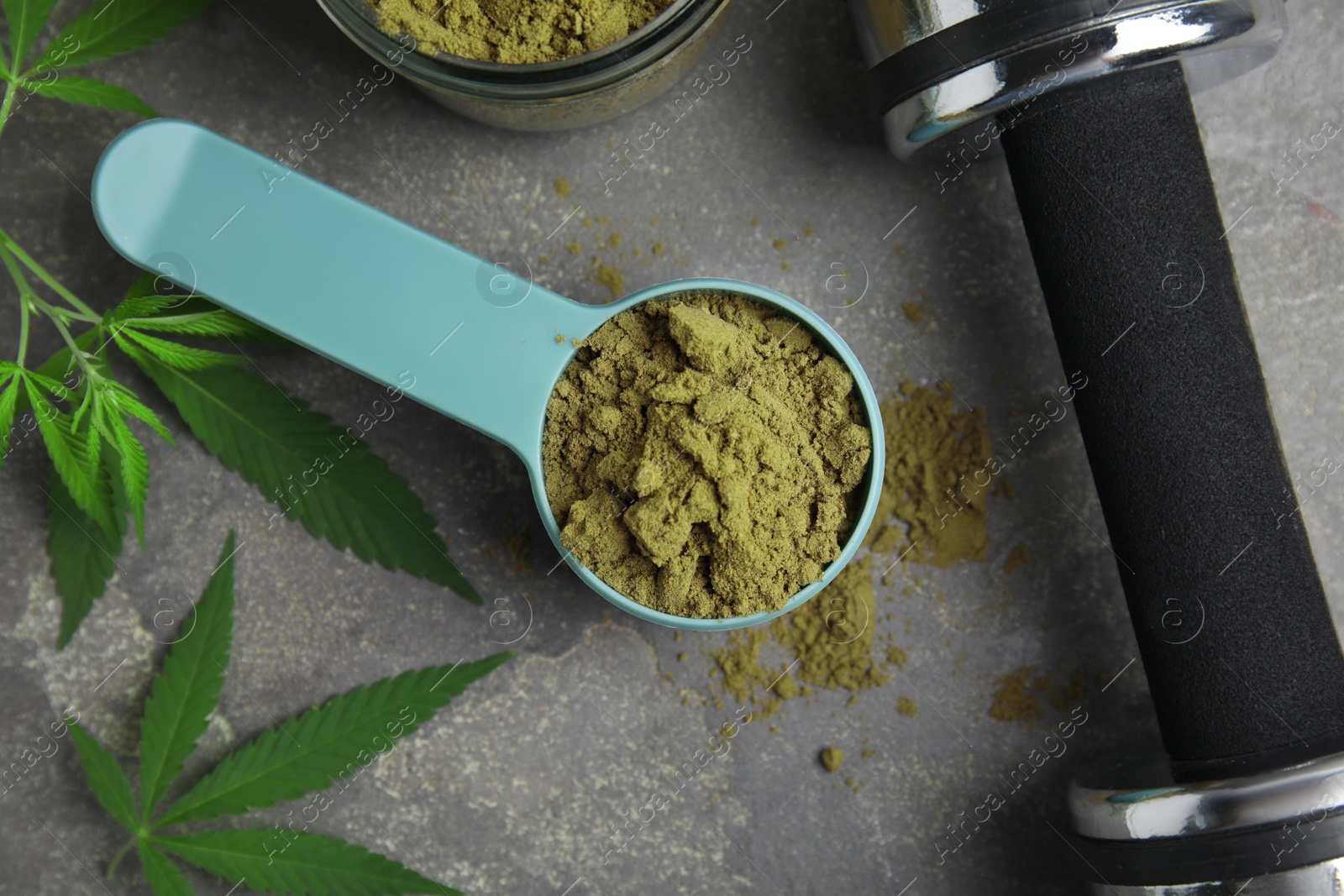 Photo of Hemp protein powder, fresh leaves and dumbbell on grey table, flat lay