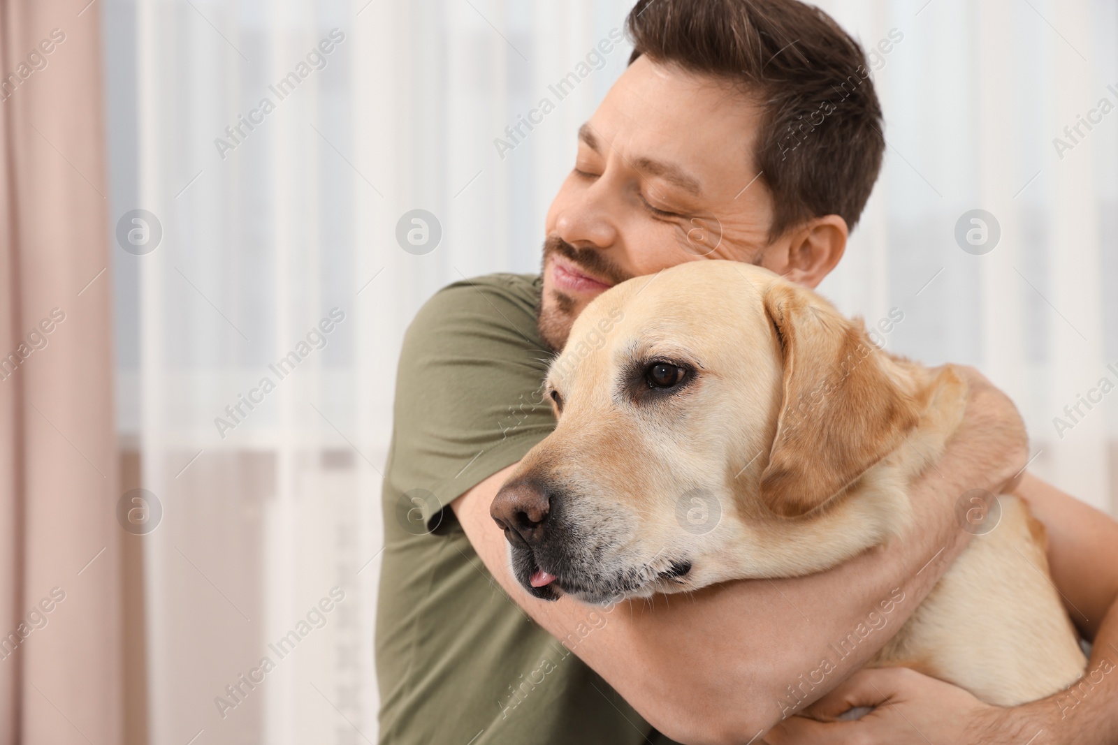 Photo of Man hugging his cute Labrador Retriever at home. Space for text