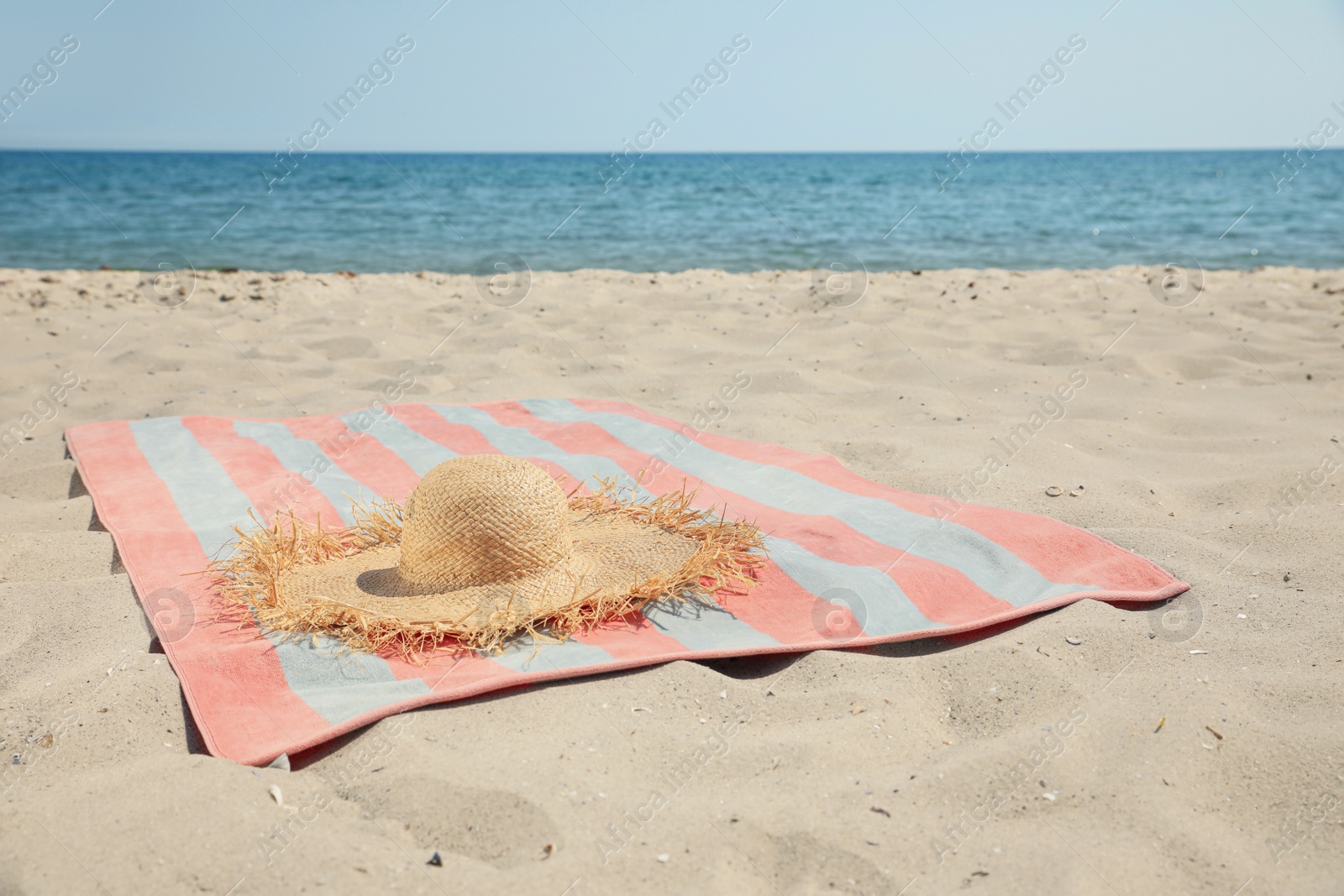 Photo of Striped beach towel with straw hat on sand near sea