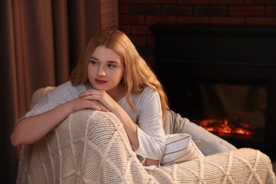 Photo of Beautiful young woman resting near fireplace at home