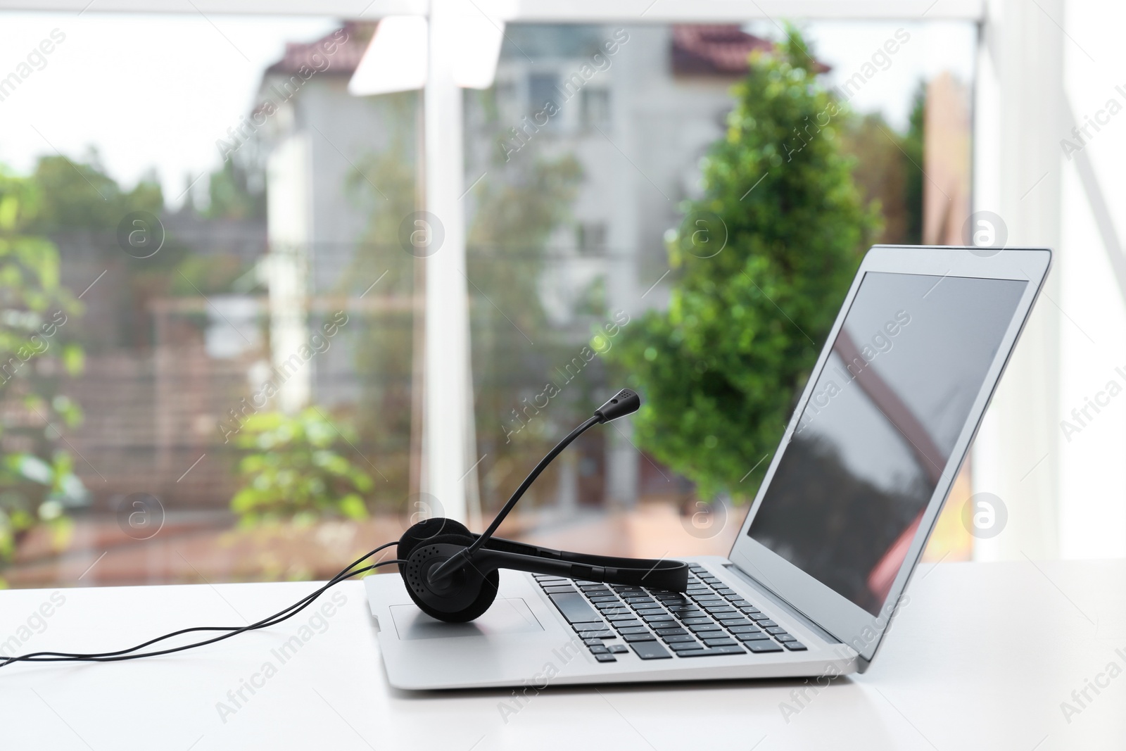 Photo of Modern laptop and headset on table indoors. Technical support concept