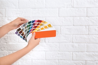 Photo of Female interior designer with color palette samples near brick wall, closeup. Space for text