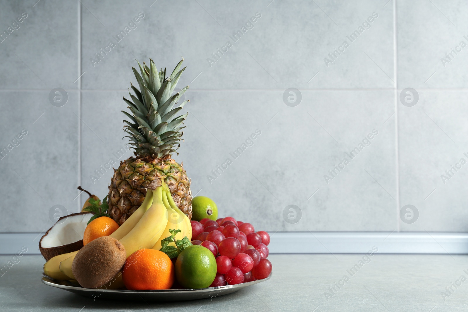 Photo of Plate with different ripe fruits on grey table. Space for text