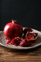 Plate with ripe pomegranates on table against black background