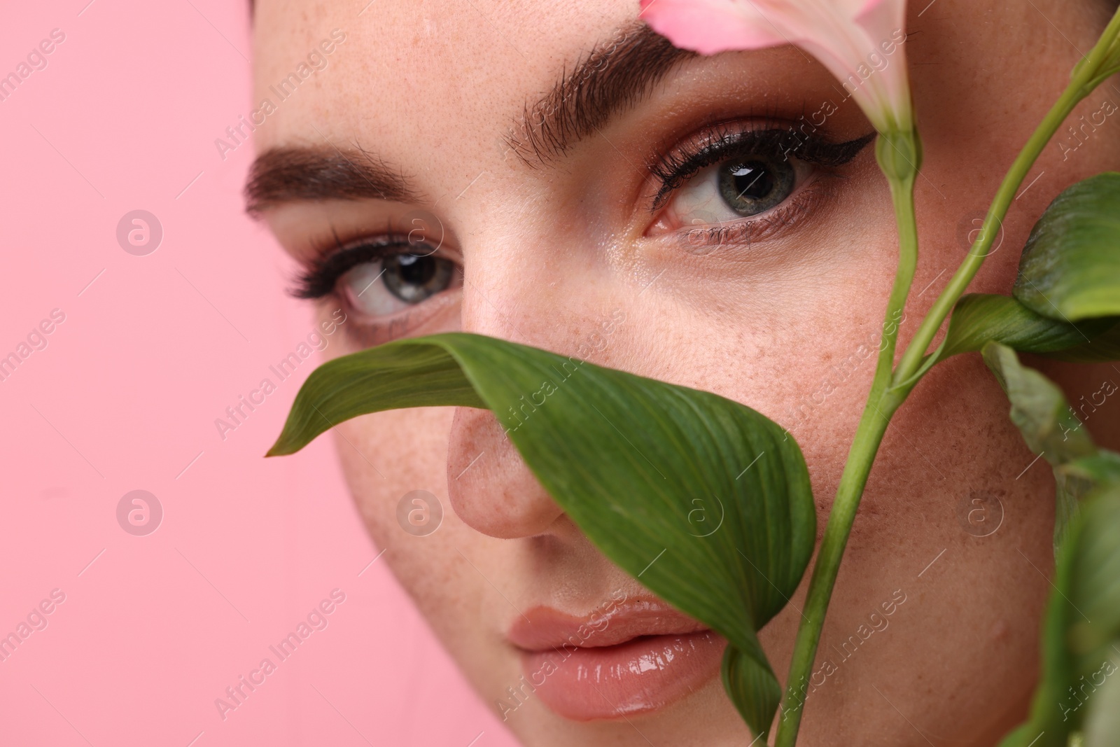 Photo of Beautiful woman with fake freckles and flower on pink background, closeup