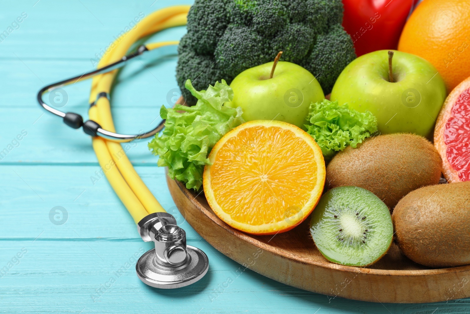 Photo of Fruits, vegetables and stethoscope on light blue wooden background, closeup. Visiting nutritionist