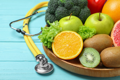 Photo of Fruits, vegetables and stethoscope on light blue wooden background, closeup. Visiting nutritionist