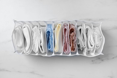 Organizer with folded women's underwear on white marble table, top view