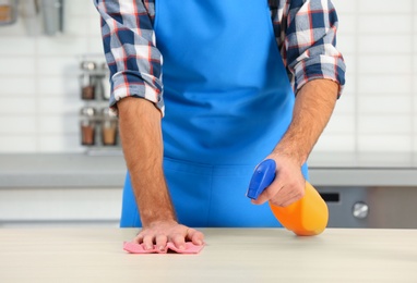 Photo of Man cleaning table with rag in kitchen, closeup