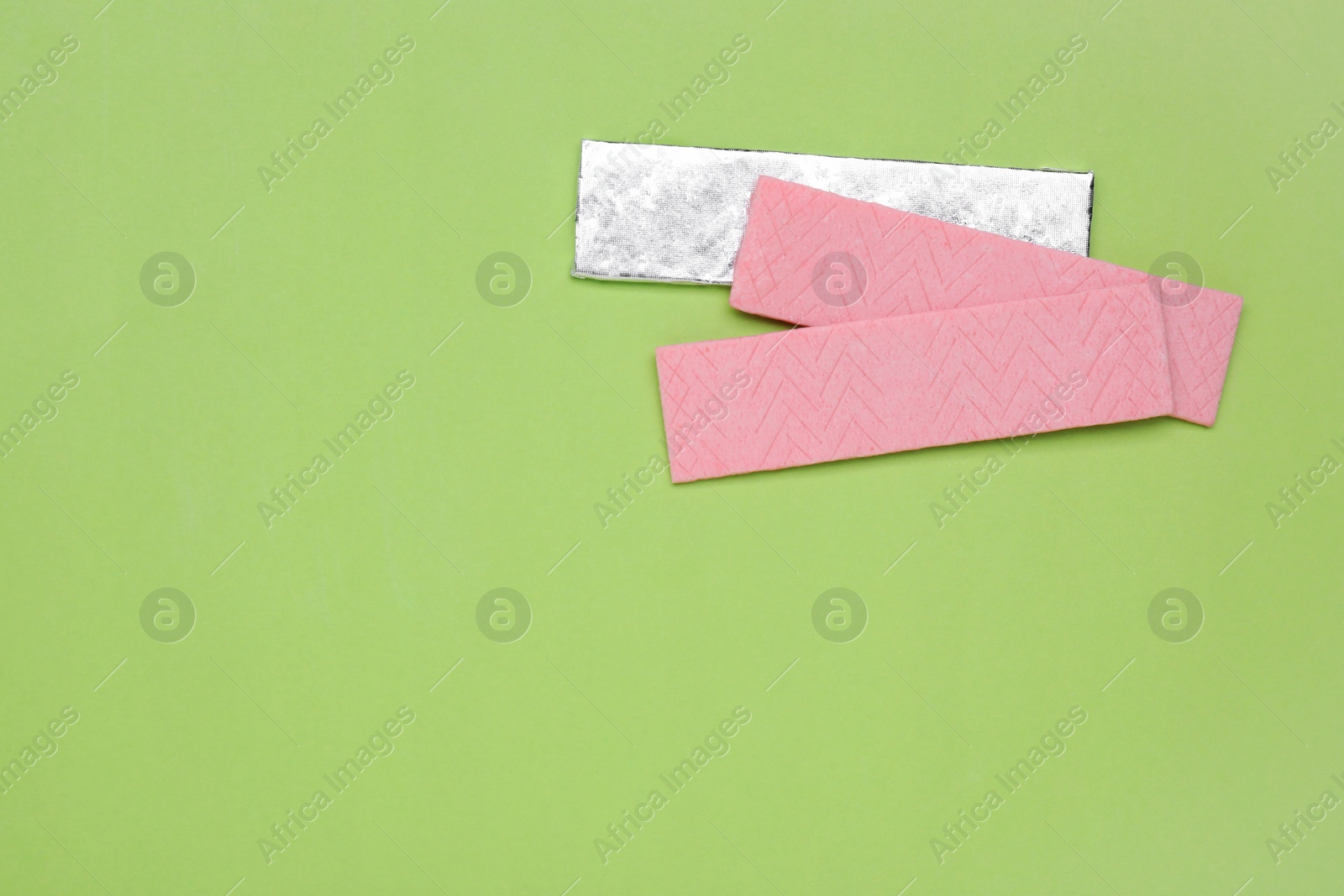 Photo of Sticks of tasty chewing gum on light green background, flat lay. Space for text