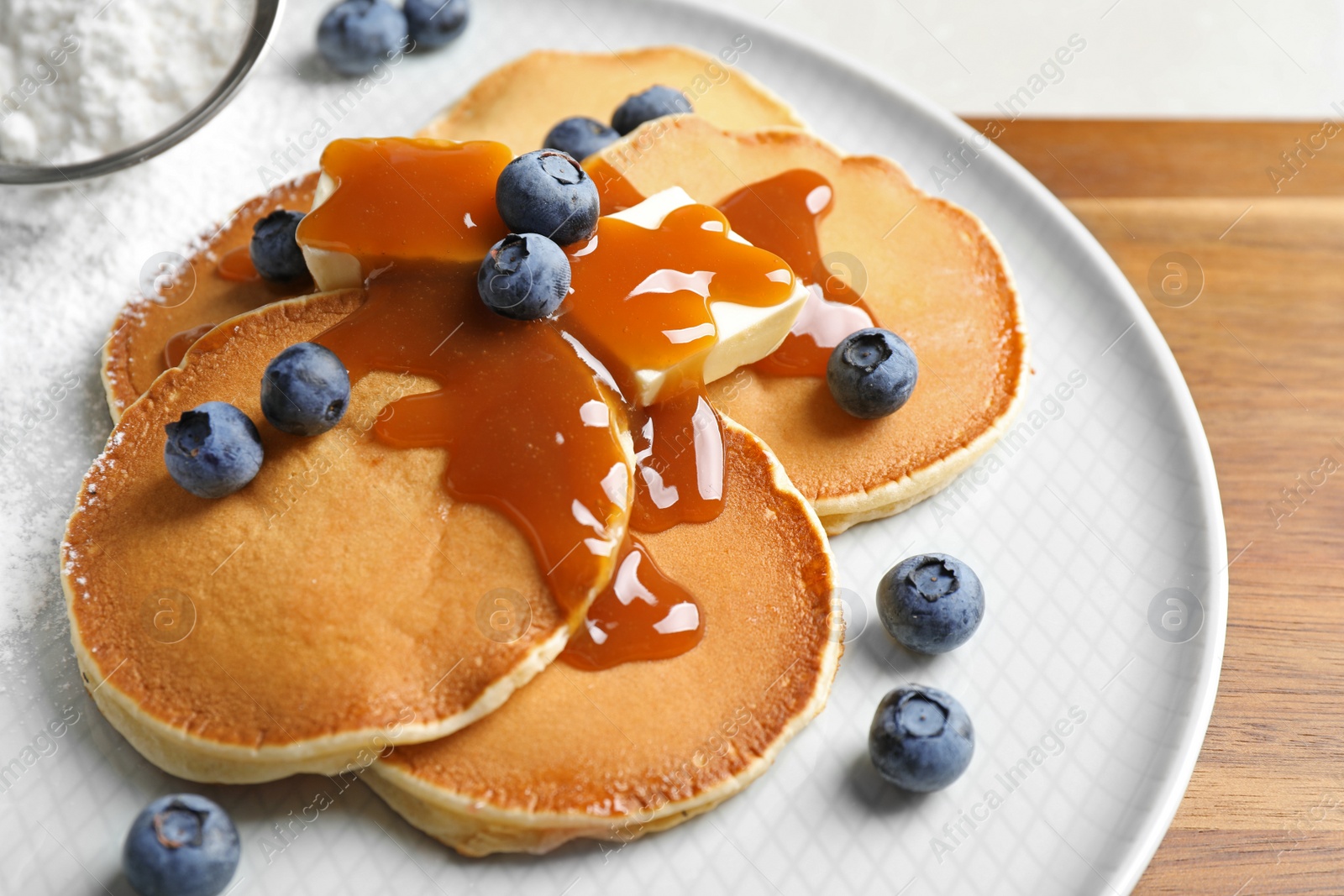 Photo of Delicious pancakes with fresh blueberries, butter and syrup on wooden table, closeup