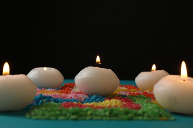 Photo of Diwali celebration. Burning candles and colorful rangoli on light blue background, closeup