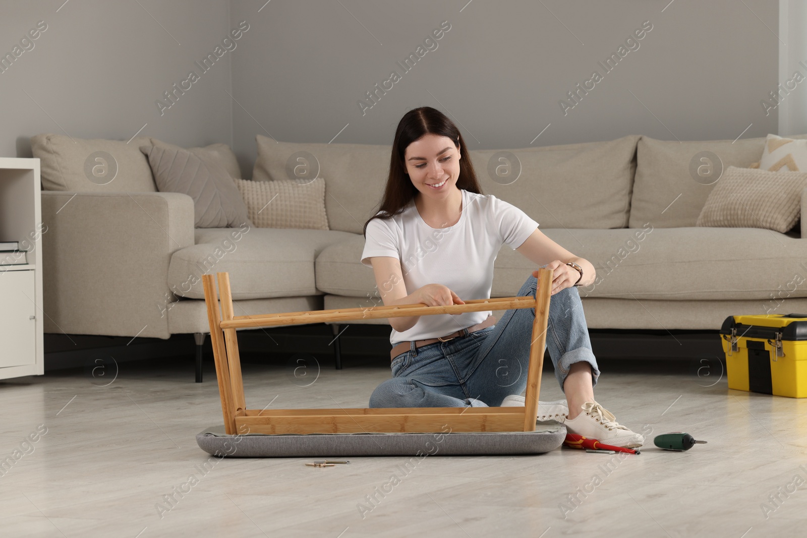 Photo of Young woman assembling shoe storage bench on floor at home