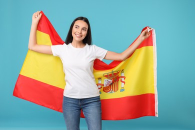 Happy young woman with flag of Spain on light blue background