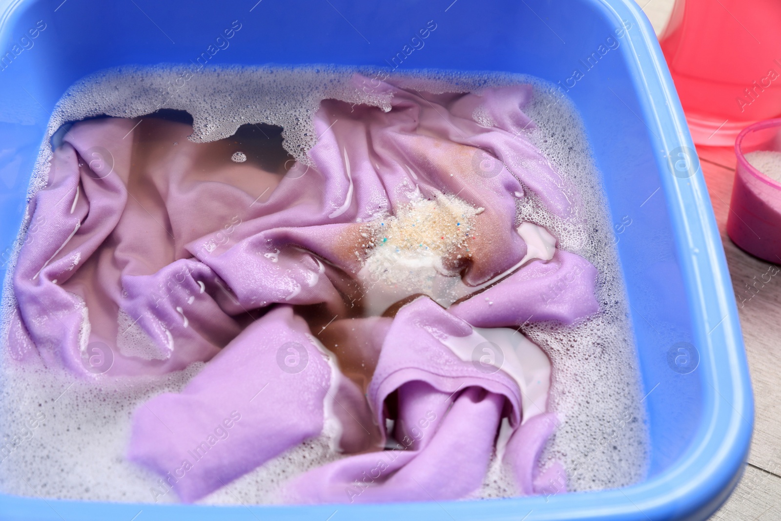 Photo of Basin with clothes in suds on white wooden surface, closeup. Hand washing laundry