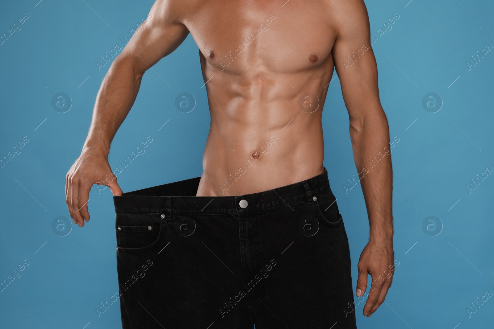 Photo of Shirtless man with slim body wearing big jeans on light blue background, closeup