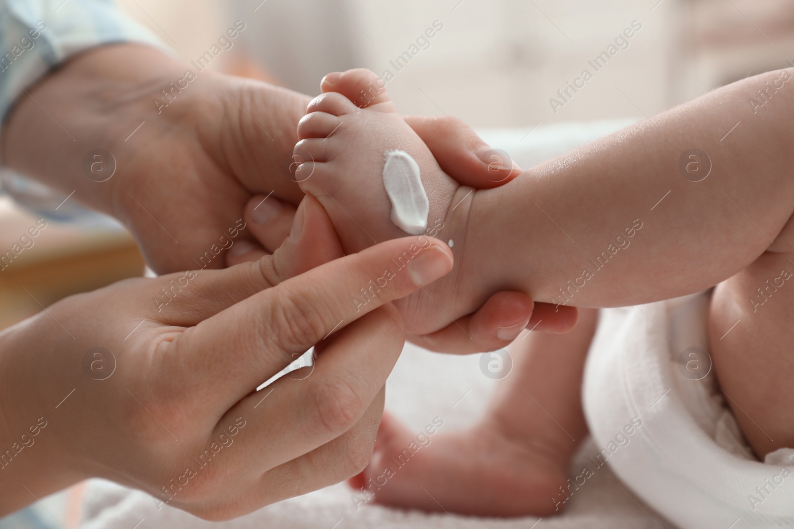 Photo of Mother applying body cream on her little baby indoors, closeup