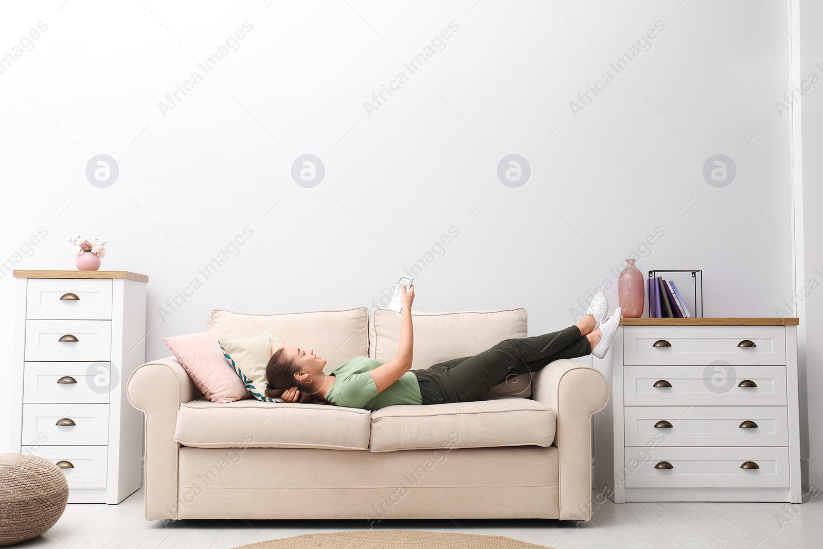 Photo of Happy young woman switching on air conditioner with remote control at home