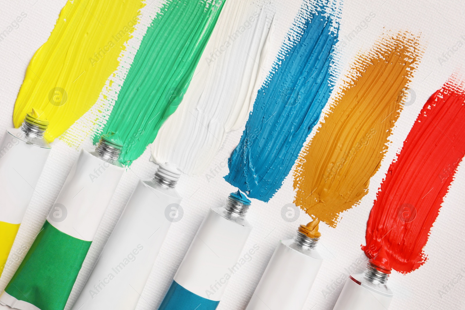 Photo of Tubes with oil paints and strokes on white canvas, flat lay