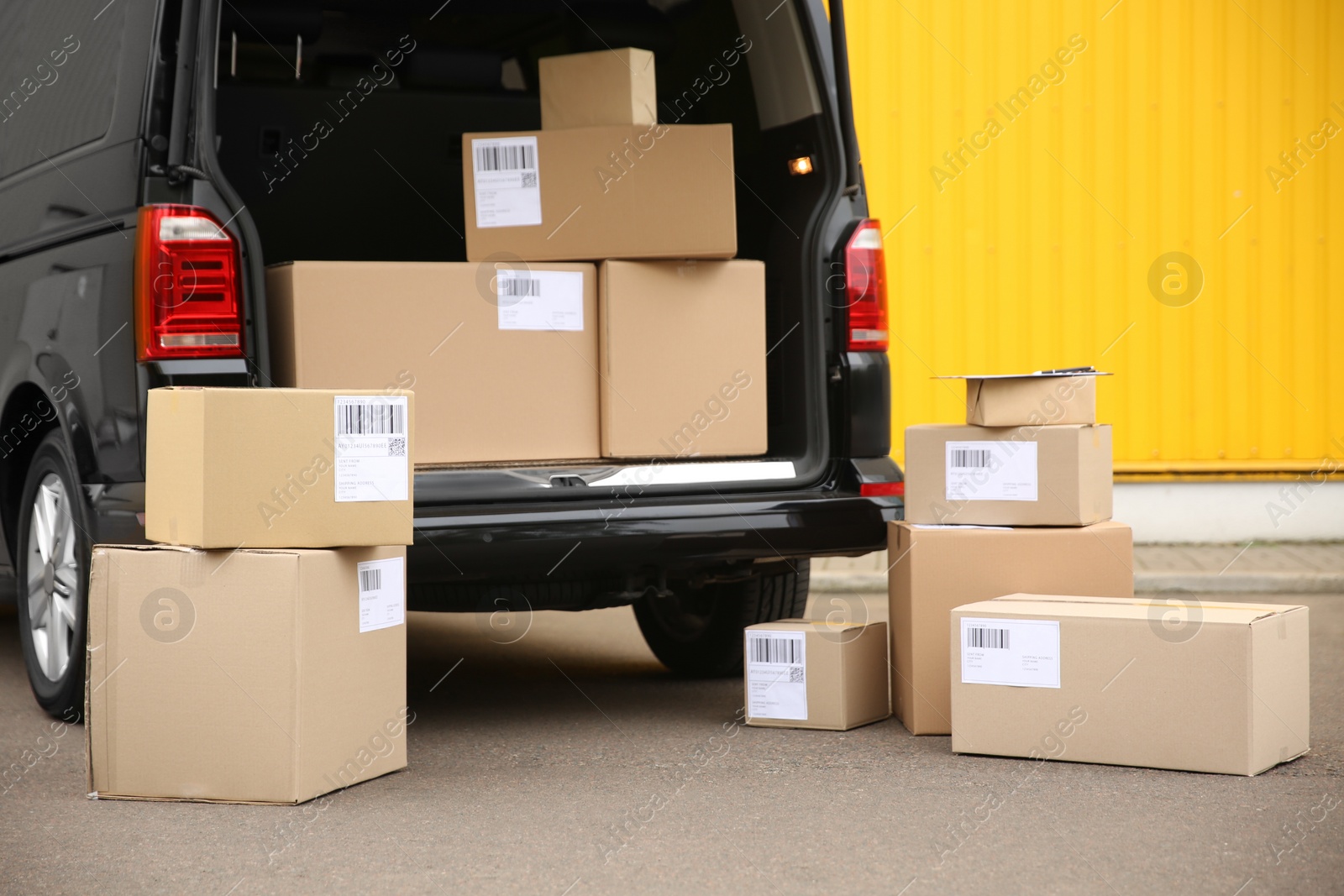 Photo of Black delivery van and many different parcels near yellow wall outdoors. Courier service