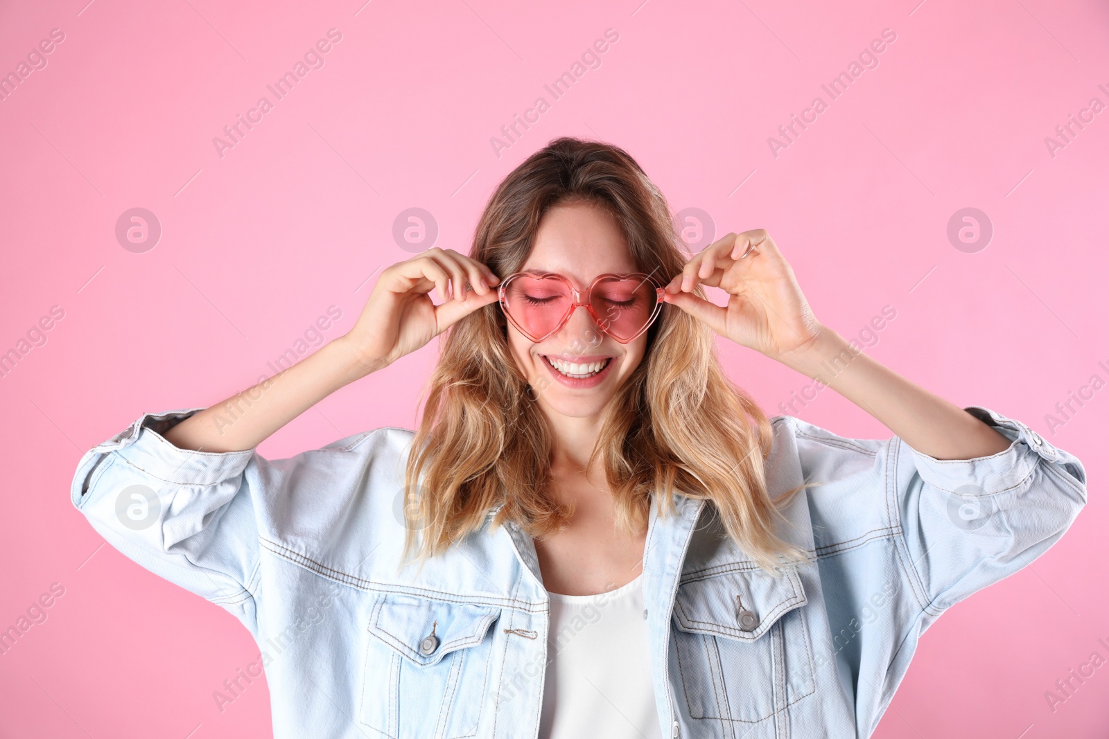 Photo of Young beautiful woman wearing heart shaped glasses on pink background