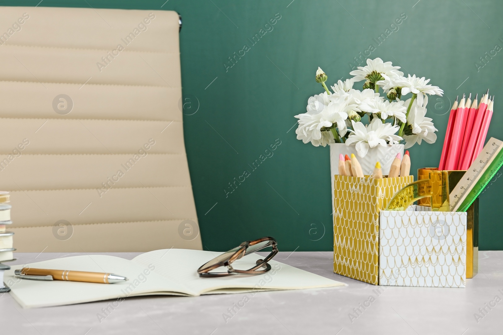 Photo of Flowers and stationery on table near chalkboard in classroom. Happy teacher's day