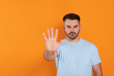 Photo of Handsome man showing stop gesture on orange background, space for text